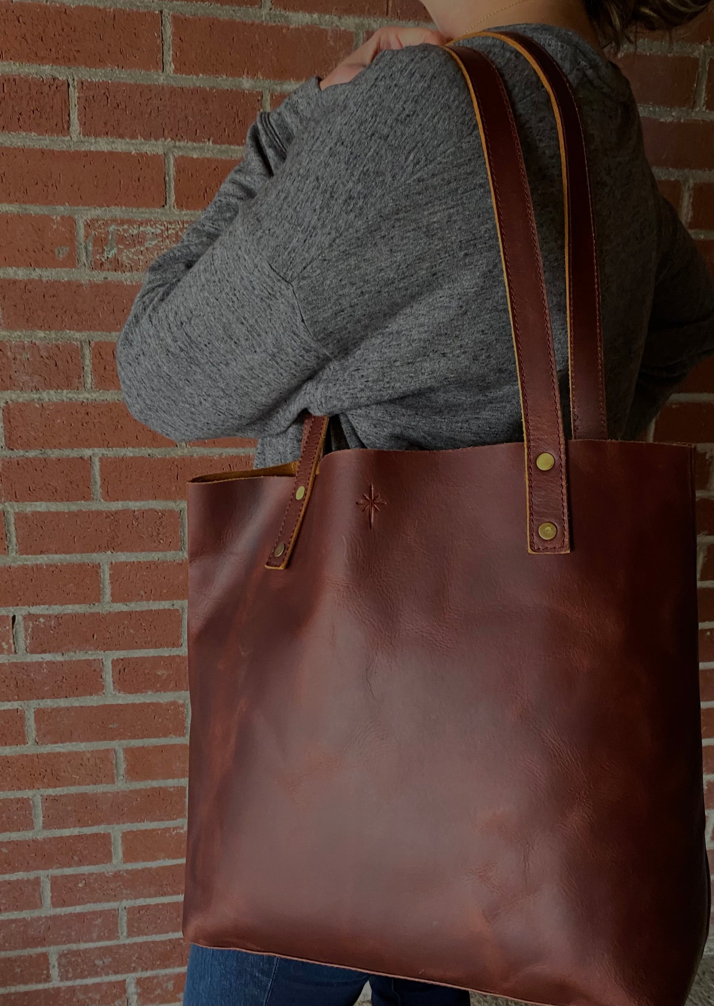Girl with brown leather tote bag on shoulder, top of bag starts  just above waist